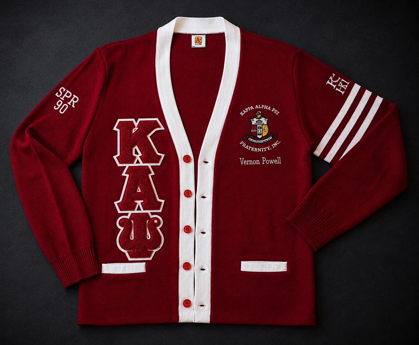 Custom crimson and white Greek letter cardigan sweater with large chenille letters, full-color heraldic crest, personalized name, sleeve embroidery, and athletic stripes.